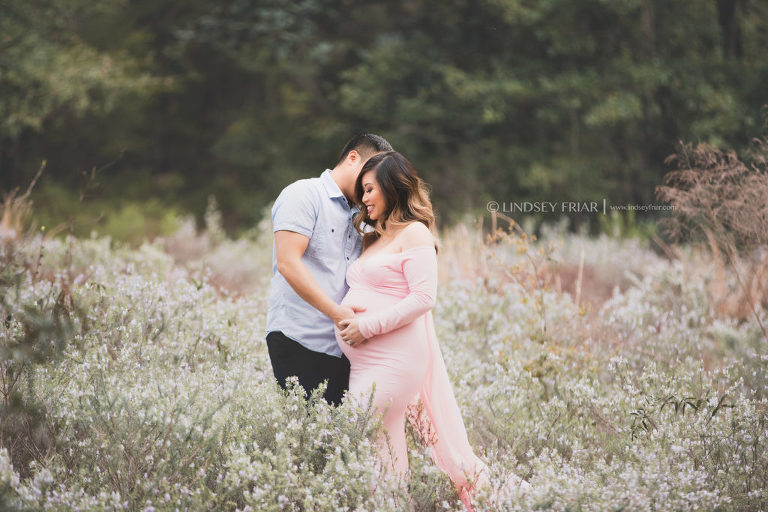 mom and dad posing in a field of flowers for a maternity session