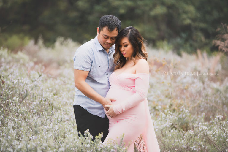 mom and dad posing together for a maternity session in a field of flowers